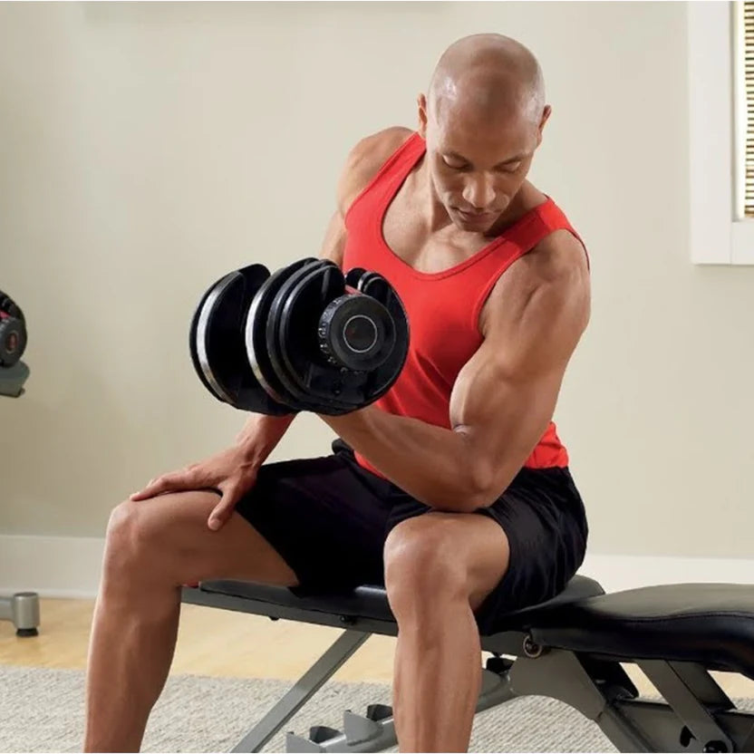 Man in red tank top and black shorts lifting dumbbells in a home gym setting.