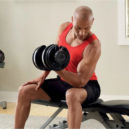 Man in red tank top and black shorts lifting dumbbells in a home gym setting.