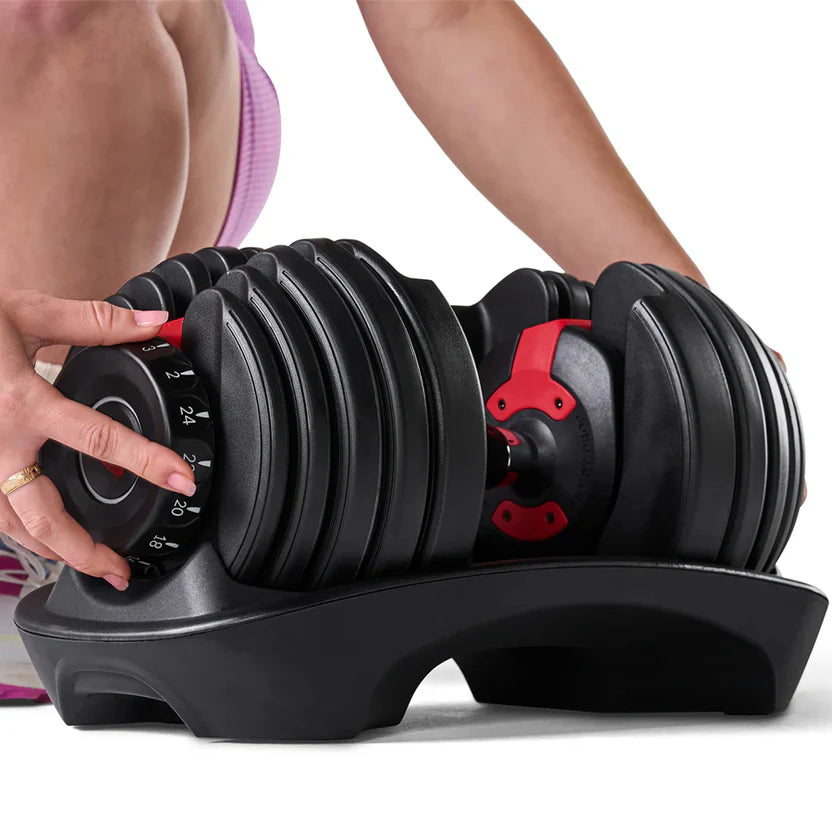 Person adjusting a black adjustable dumbbell with red accents on a white background